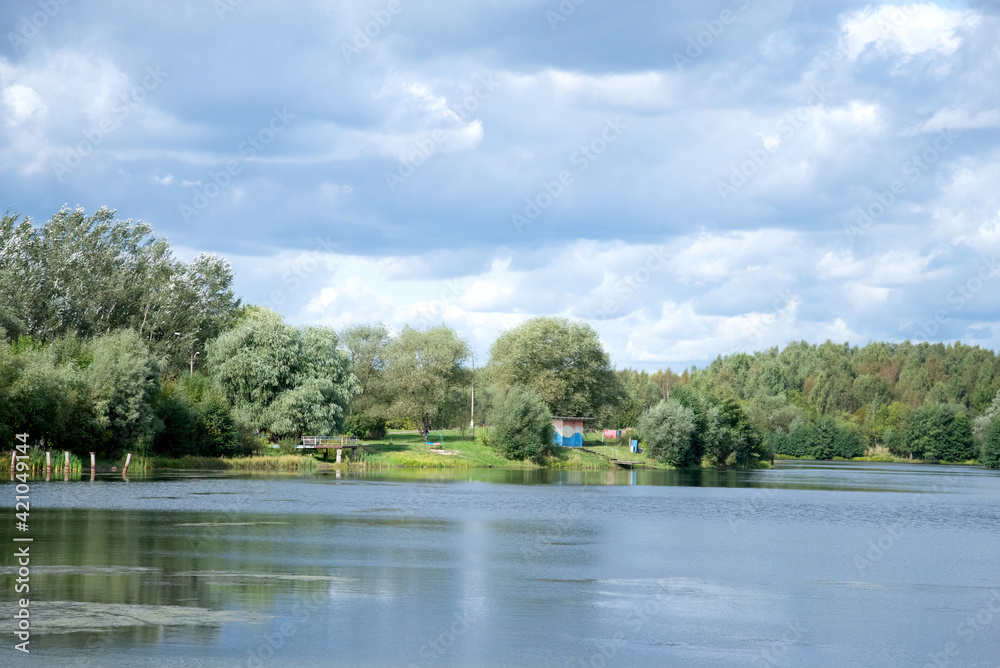 Summer lake landscape with blue cloudy sky green trees and bushes on horizon