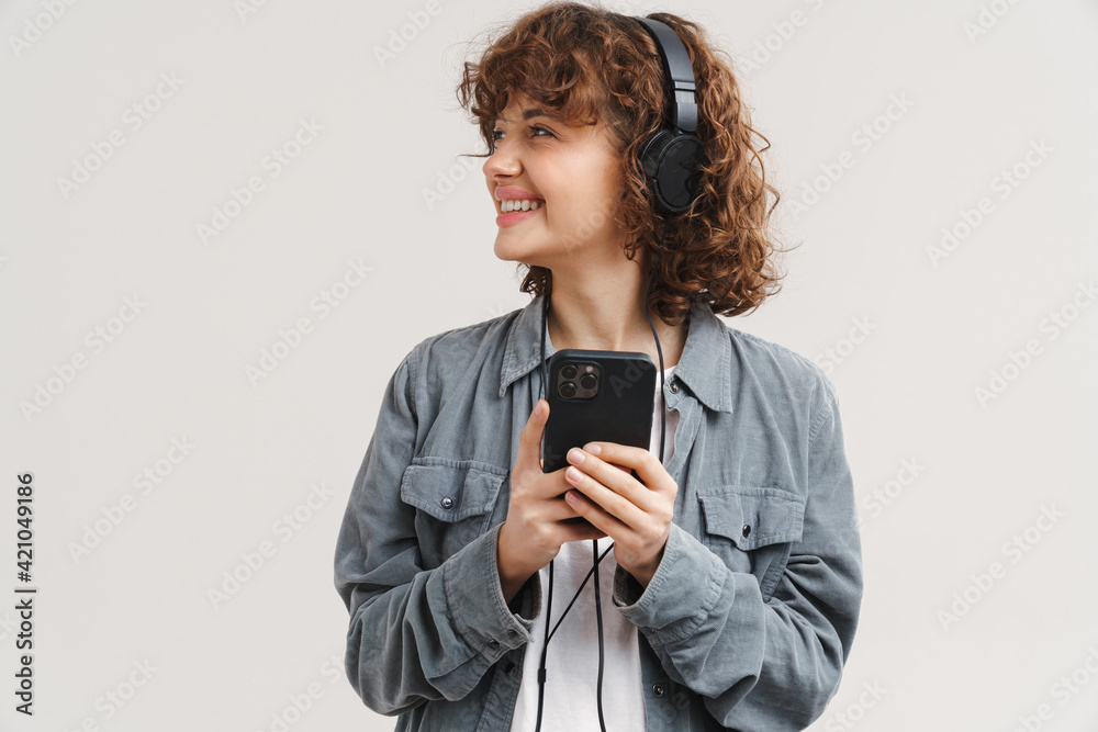 Fototapeta premium Young ginger joyful woman listening music with headphones and cellphone
