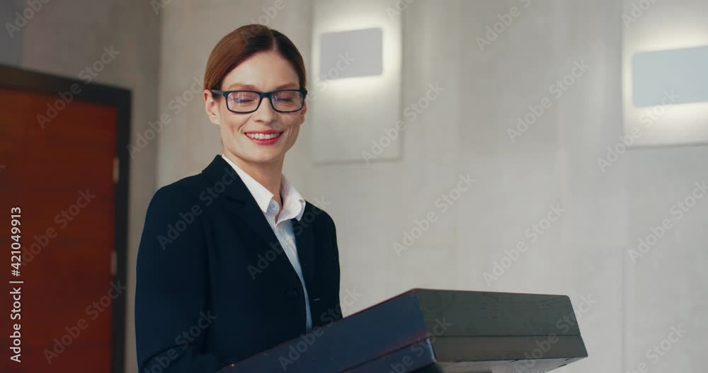 Young successful smart business lady in suit and glasses standing behind podium and looking at camera smilling. Young successful smart business lady in suit and glasses standing behind podium and looking at camera smilling.