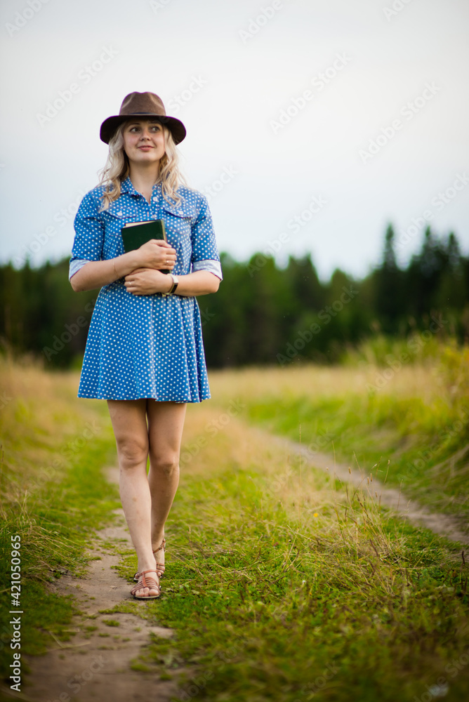 blonde girl in a blue dress and hat reads a book in nature, selective focus