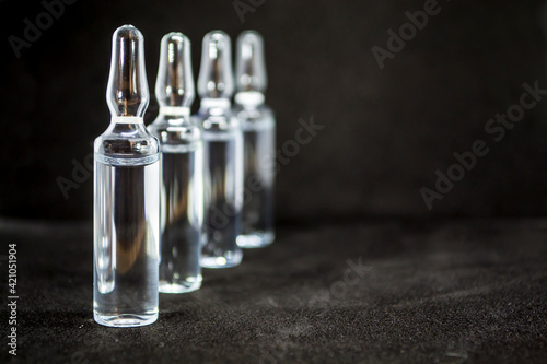 Glass medical ampoule vial for injection. Medicine is liquid sodium chloride with of aqueous solution in ampulla. Close up. Bottles ampule multicolor on background color and water. Human plasma.
