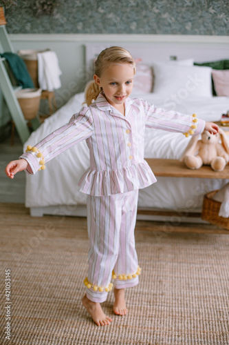 Child girl blonde with blue eyes in pajamas is dancing Bedroom in the house Stylish interior