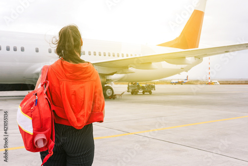 The girl is standing near the plane waiting for departure. Boarding passengers on the flight. Young traveler at the airport. Travel and tourism concept