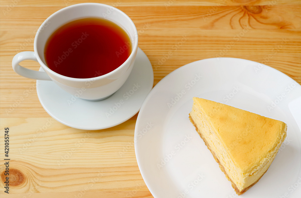 Cup of Hot Tea with a Plate of Baked Cheesecake Served on Wooden Table Cup of Hot Tea with a Plate of Baked Cheesecake Served on Wooden Table