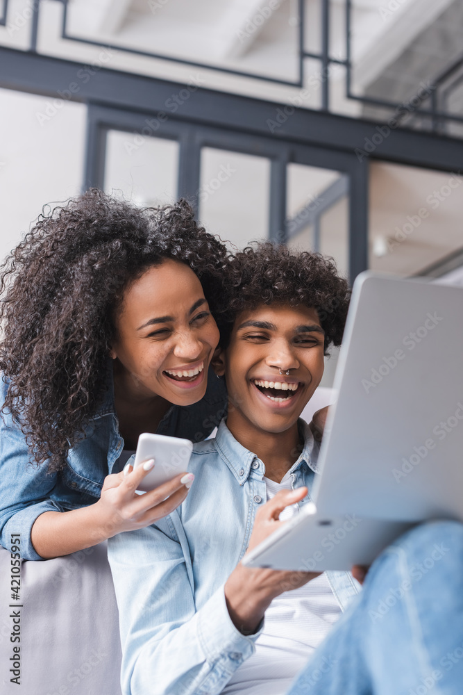 Positive african american couple with smartphone and laptop at home