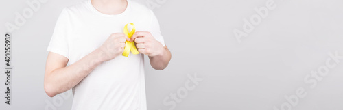 Young man in white t-shirt holding yellow ribbon awareness symbol for suicide, sarcoma bone cancer, bladder cancer, liver cancer and childhood cancer concept. Health care. Copyspace.