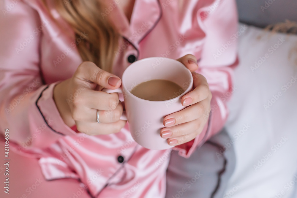 Young woman holding a pink mug with coffee in her hands Pink pajamas in the apartment Painted nails Young woman holding a pink mug with coffee in her hands Pink pajamas in the apartment Painted nails