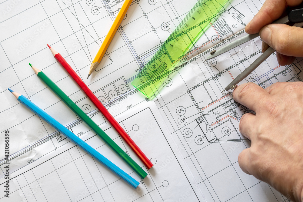 The draughtsman uses a compass to determine the size on the ruler. The porous texture of the drawing paper. Graphite and coloured pencils lie on the drawing The draughtsman uses a compass to determine the size on the ruler. The porous texture of the drawing paper. Graphite and coloured pencils lie on the drawing