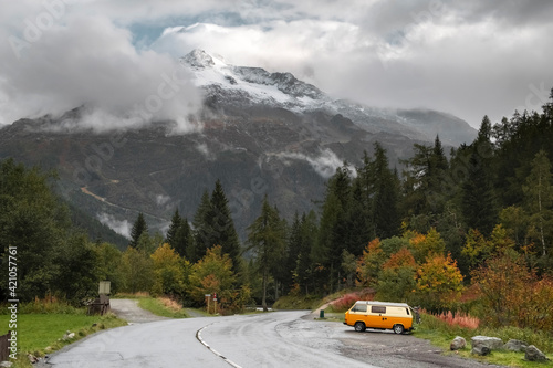 A yellow van is parked for the night on the side of the road with a view of the French Alps