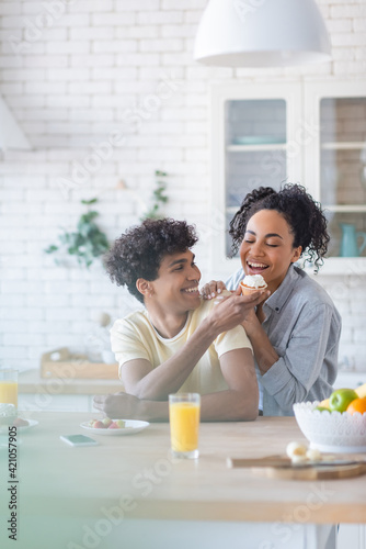 Smiling african american man feeding girlfriend with cupcake in kitchen