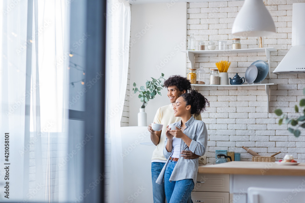 Smiling african american man with cup hugging girlfriend in kitchen Smiling african american man with cup hugging girlfriend in kitchen