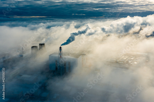 large clouds of white smoke cover power plant territory under bright sunlight on frosty winter day aerial view