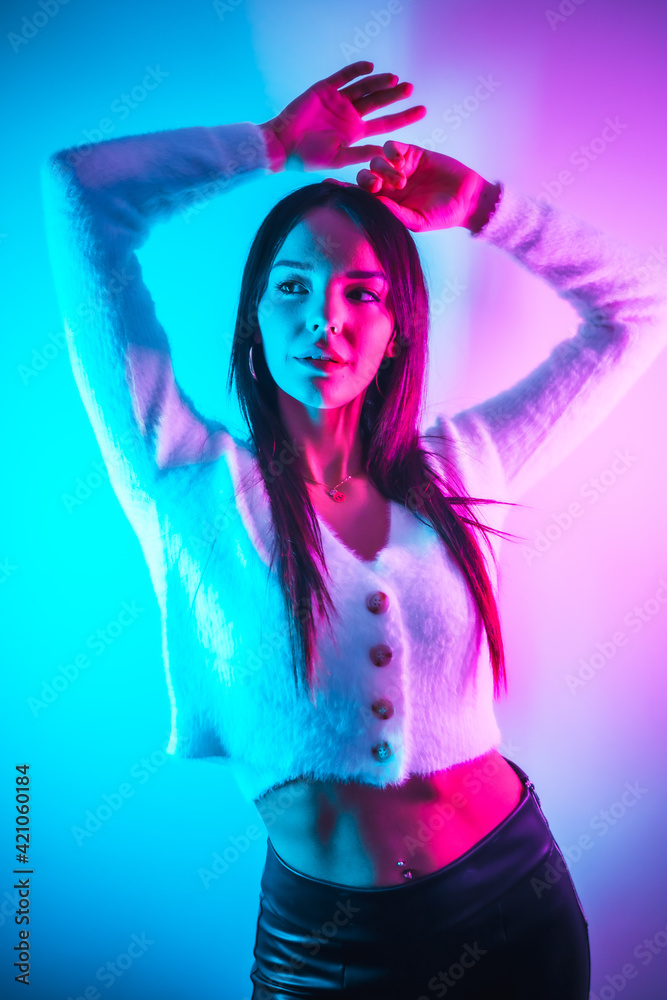 Party lifestyle in a nightclub with pink blue neon lights, portrait of a young brunette Caucasian woman in a white wool sweater