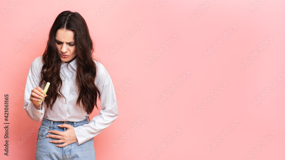 Studio shot of a young girl experiencing pain from menstruation with a tampon in her hands. Space for text. The concept of feminine hygiene. Studio shot of a young girl experiencing pain from menstruation with a tampon in her hands. Space for text. The concept of feminine hygiene.