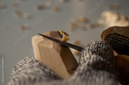 Fotografie Hands carving wood with pocket knife, wood shavings and gloves