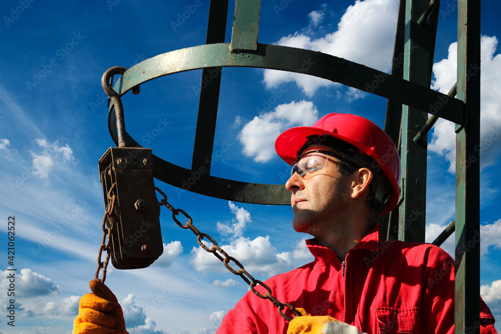 Obraz Oil rig worker with red hard hat using chain block at oil and gas