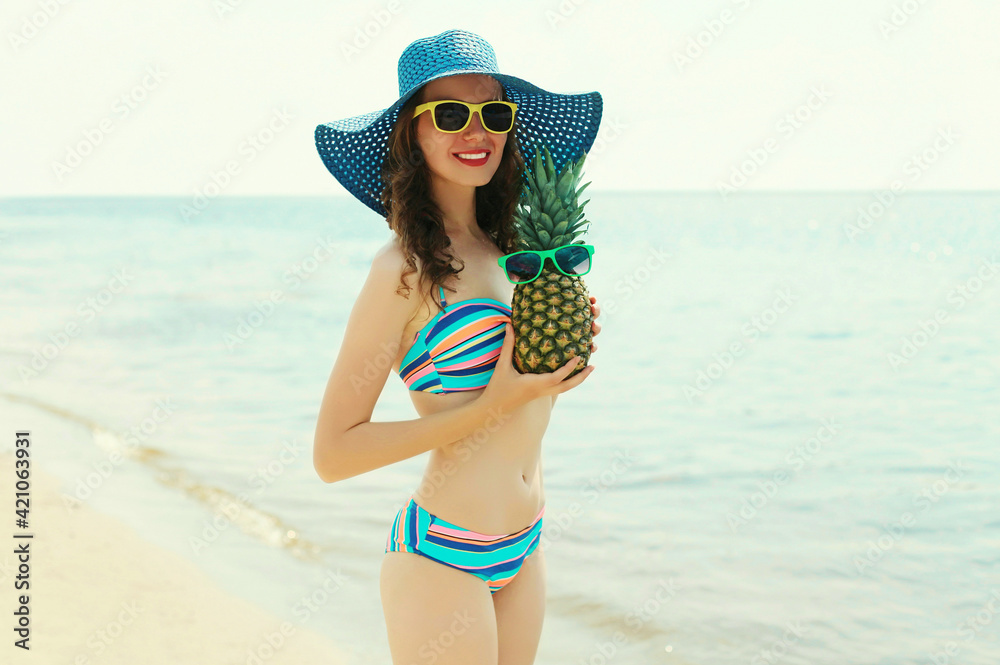 Portrait of happy smiling young woman on a beach with funny pineapple wearing a straw hat