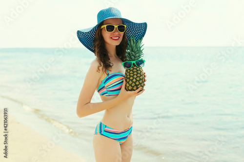 Portrait of happy smiling young woman on a beach with funny pineapple wearing a straw hat