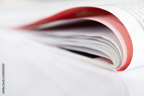 Folded magazine with red page reflected on a white surface with narrow depth of field