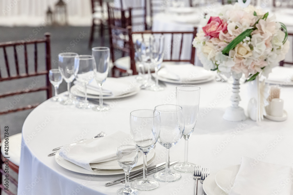 Fancy table set for dinner with flower composition in restaurant, luxury interior background. Wedding elegant banquet decoration and items for food arranged by catering service on white table.