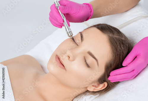 Cosmetologist makes  procedure microdermabrasion on the face against acne and blackheads near the eyes. Women's cosmetology in the beauty salon.