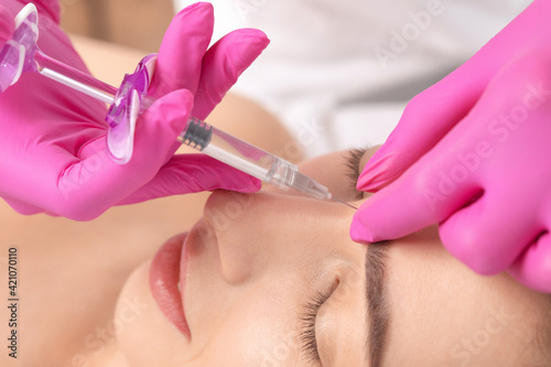 The doctor does injections to correct the hump on the nose with the beauty of the blonde. The beautician doees injections against wrinkles on the face. Women's cosmetology in a beauty salon.
