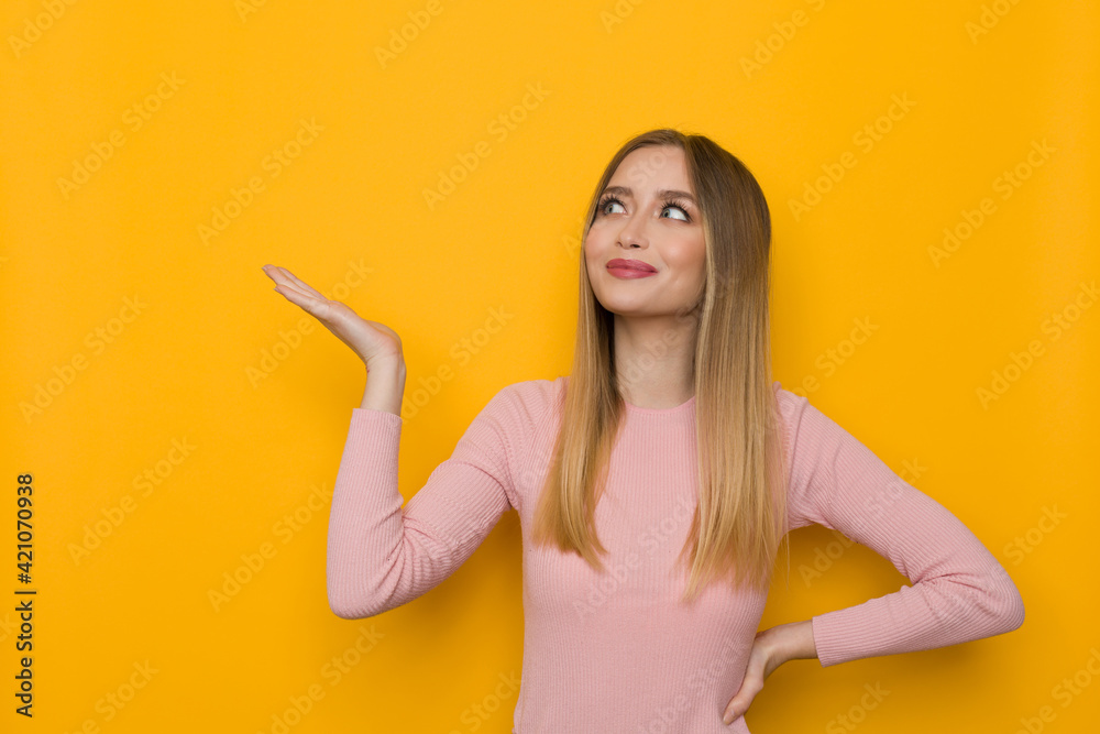 Smiling Young Woman Is Holding Hand Raised, Showing Something And Looking Up