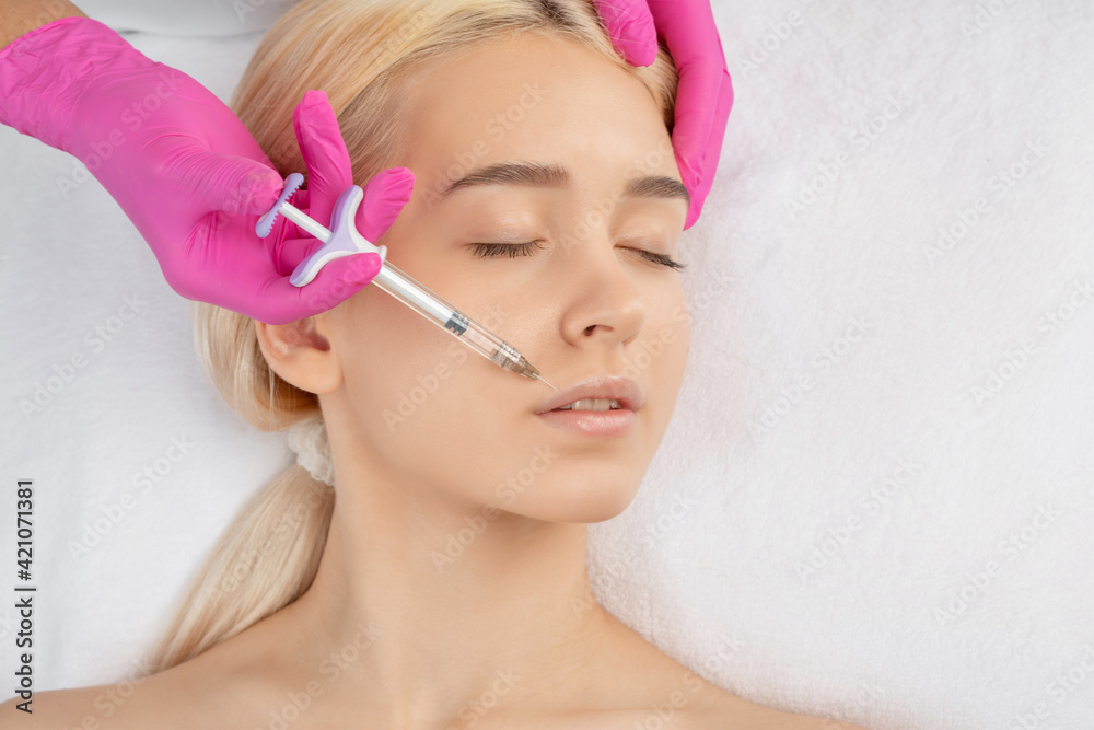 Cosmetologist does injections for lips augmentation and anti wrinkle in the nasolabial folds of a beautiful woman. Women's cosmetology in the beauty salon. Cosmetologist does injections for lips augmentation and anti wrinkle in the nasolabial folds of a beautiful woman. Women's cosmetology in the beauty salon.