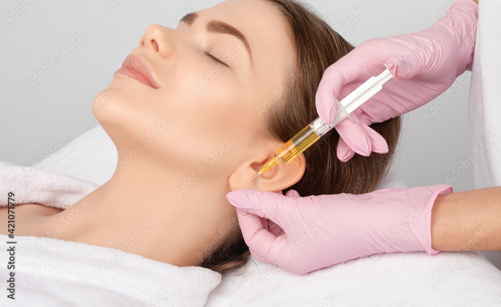 The doctor cosmetologist makes the injections procedure for smoothing wrinkles and against flabbiness of the skin on earlobe of a beautiful, young woman.Women's cosmetology in the beauty salon. The doctor cosmetologist makes the injections procedure for smoothing wrinkles and against flabbiness of the skin on earlobe of a beautiful, young woman.Women's cosmetology in the beauty salon.