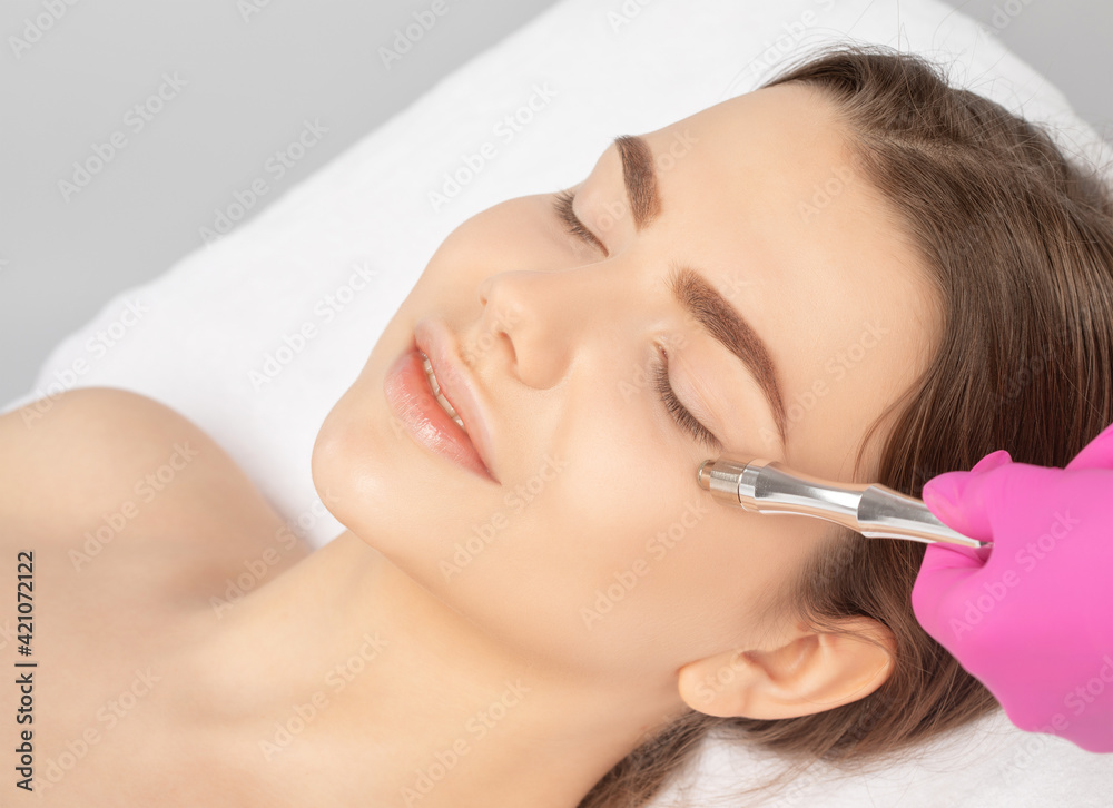 The cosmetologist makes the procedure Microdermabrasion of the face skin of a beautiful girl in a beauty salon.Cosmetology and professional skin care. The cosmetologist makes the procedure Microdermabrasion of the face skin of a beautiful girl in a beauty salon.Cosmetology and professional skin care.