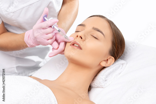 Cosmetologist does injections for lips augmentation and anti wrinkle in the nasolabial folds of a beautiful woman. Women's cosmetology in the beauty salon.