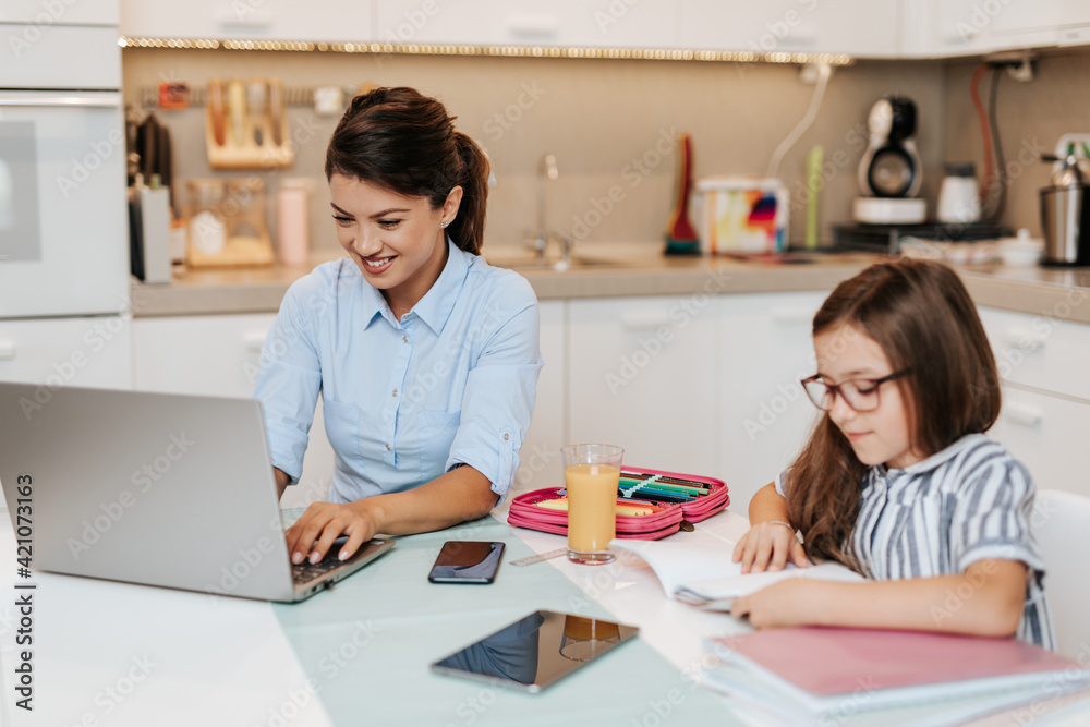 Mother works from home due to coronavirus while her daughter does her homework. Mother works from home due to coronavirus while her daughter does her homework.