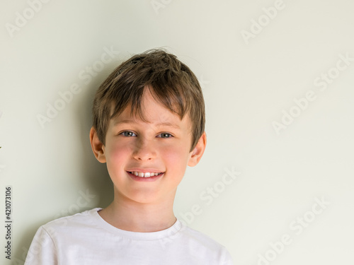 Portrait of smiling 8 year old boy wearing white t-shirt against gray wall with copy space
