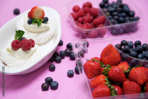 Strawberries  raspberries and blueberries arranged in containers with a dessert of meringue  cream and berries to the side. Arranged on a pink tablecloth