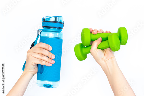 Sports blue water bottle and two green dumbbells in a woman's hand isolated on white background. Sport equipment. Fitness concept, healthy lifestyle photo