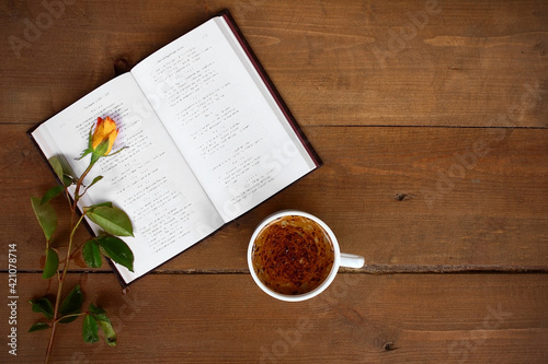 On a wooden background, an open book, next to a rose and a cup of coffee.
