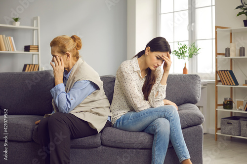 Family conflict, misunderstanding and bad relationship drama of different generations. Elderly mother and grown up daughter after quarrel sitting on couch separately ignoring avoiding communication