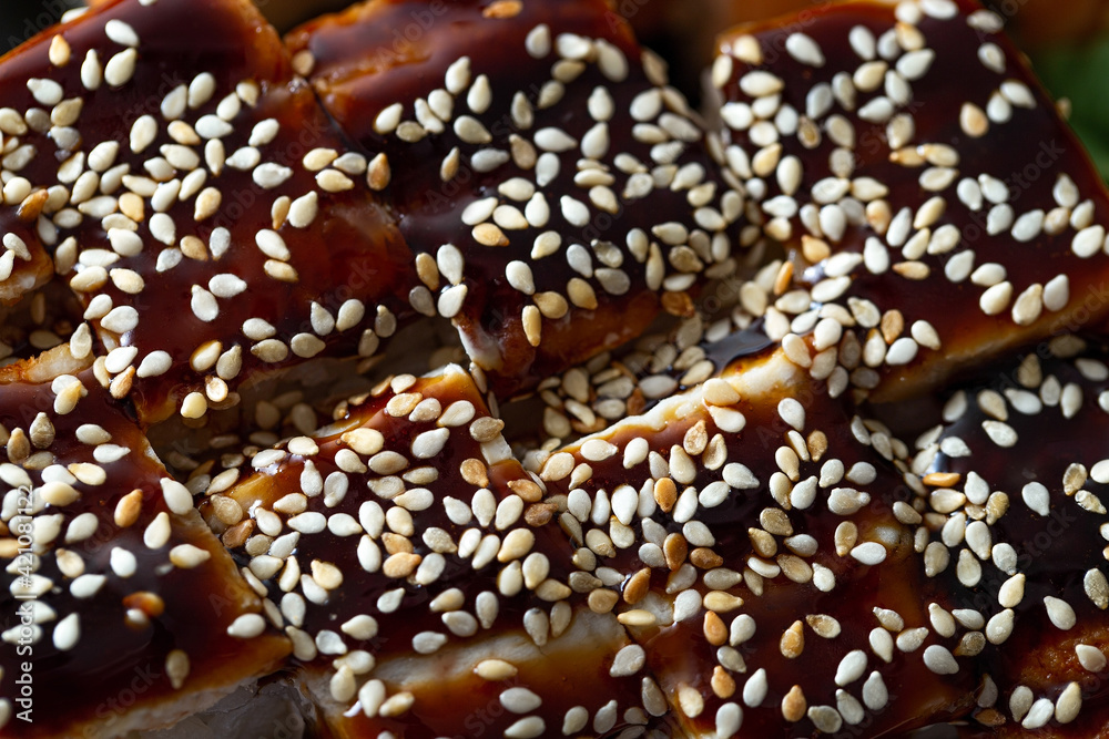A tray with an assortment of freshly prepared rolls with eel, sesame seeds and sweet soy sauce. Food from the delivery service close-up. Asian cuisine