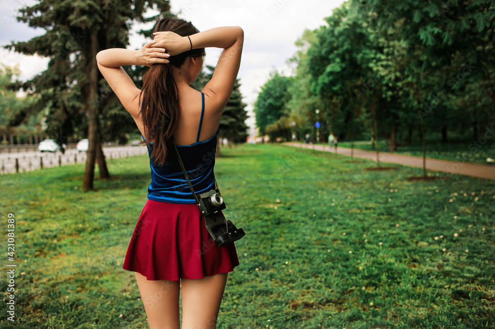 Teen Girl in a short skirt Travels With Camera on the back in nature on a  sunny summer day Stock Photo | Adobe Stock