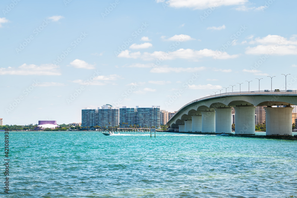 Beach in city of Sarasota, Florida on sunny day with cityscape and bay buildings by John Ringling causeway bridge in summer