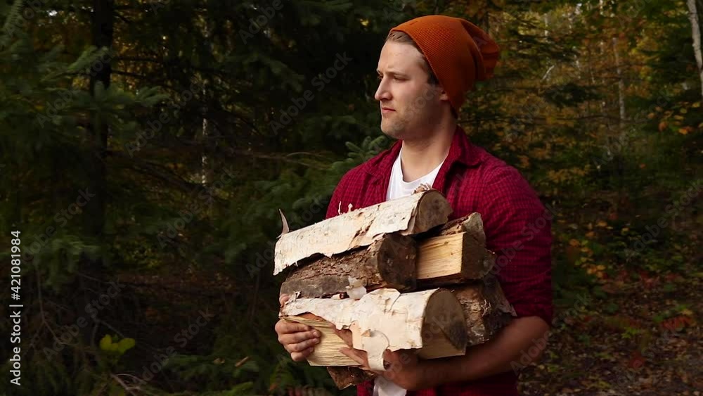 Handsome young man carrying a large pile of wood while camping in the beautiful countryside of Canada during the fall season. Handsome young man carrying a large pile of wood while camping in the beautiful countryside of Canada during the fall season.