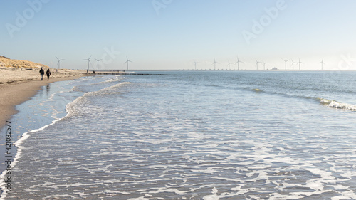 people walking on the beach of Westenschouwen in The Netherlands with hightide and with the Oosterscheldekering with windmills in the background photo