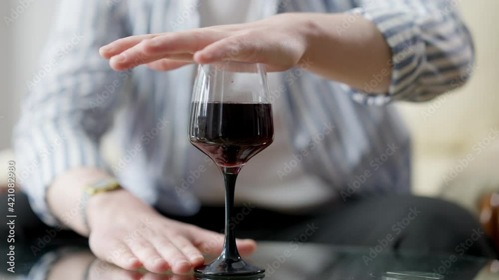 Male hand covering glass with red wine standing on glass table. Unrecognizable young Caucasian man fighting alcohol addiction. Symbol of recovery.