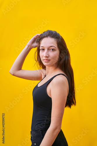 Vertical photo of a caucasian woman touching her hair and looking at camera, on yellow plain background