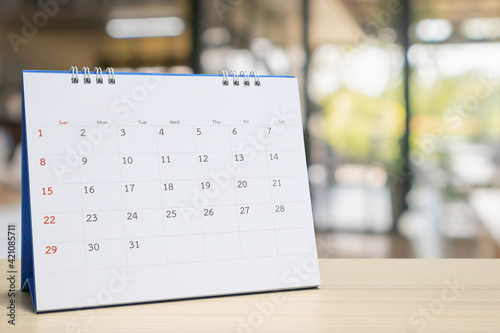 white paper desk calendar on wood table with blurred bokeh background appointment and business meeting concept