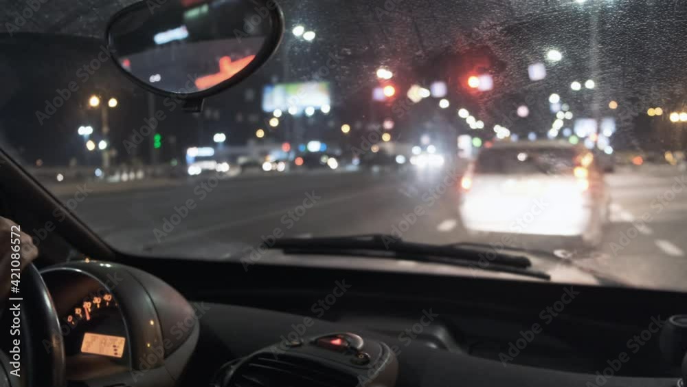 Car moves in city traffic at night, close-up. View from windshield of car front panel. Blurred bokeh of urban view streets, lights, headlights. Later return home after work. Busy town roads in evening Car moves in city traffic at night, close-up. View from windshield of car front panel. Blurred bokeh of urban view streets, lights, headlights. Later return home after work. Busy town roads in evening
