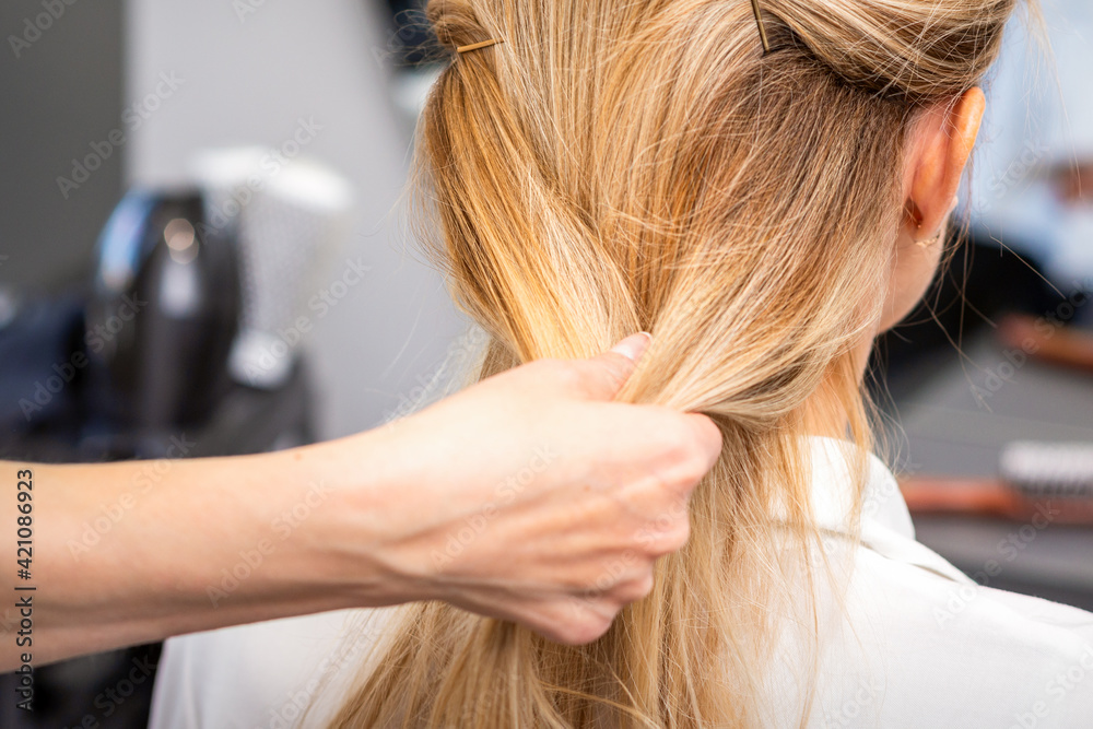 Fototapeta premium Close up of hands of female hairdresser styling hair of a blonde woman in a hair salon