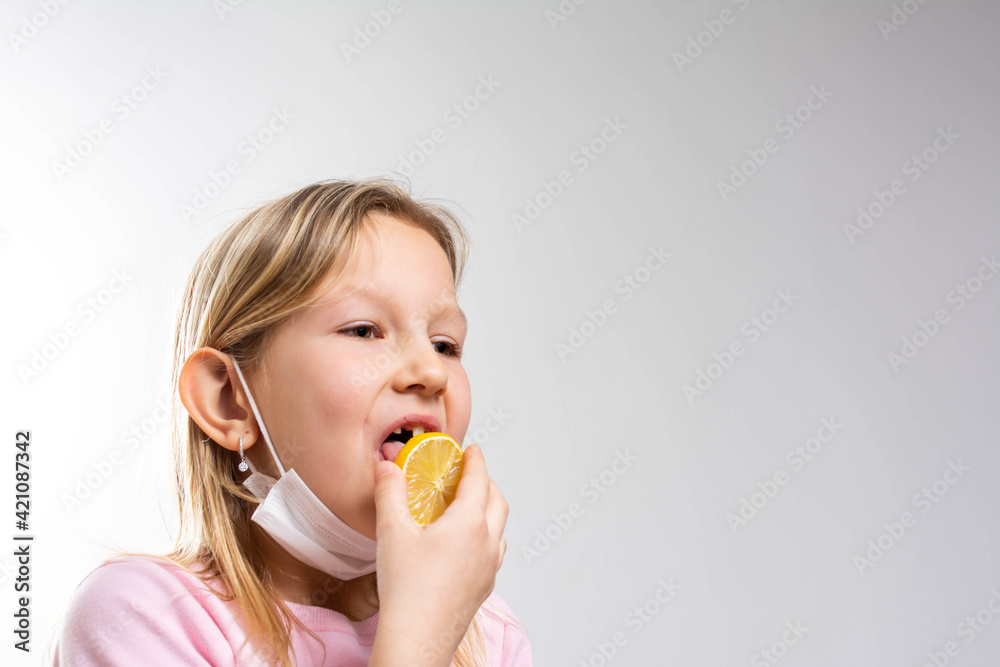 Beautiful smiling little girl with a lemon isolated on white background. Girl's Reaction to a Slice of very Sour Lemon with face mask.