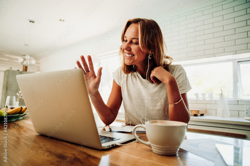 Caucasian female student on video call with friends typing on laptop sipping hot coffee working in kitchen Caucasian female student on video call with friends typing on laptop sipping hot coffee working in kitchen