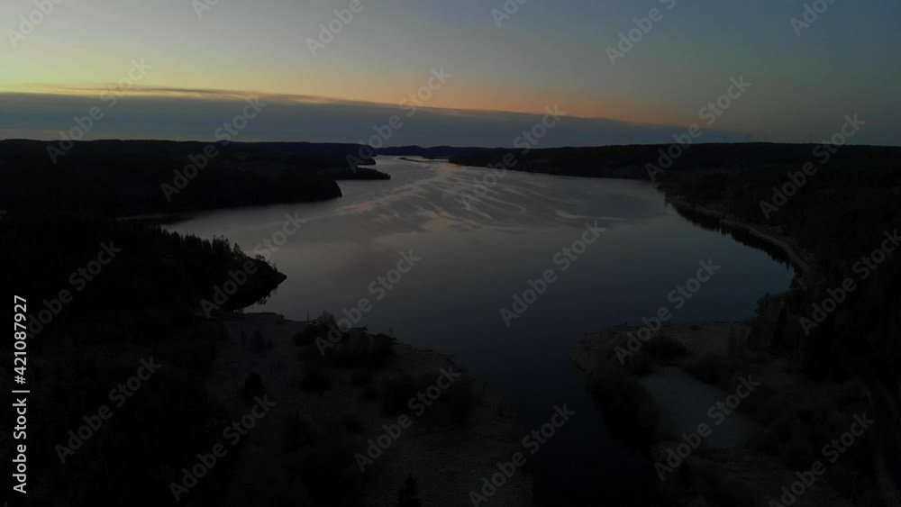 Drone view of large open lake surrounded by trees dark shadows sun setting Drone view of large open lake surrounded by trees dark shadows sun setting